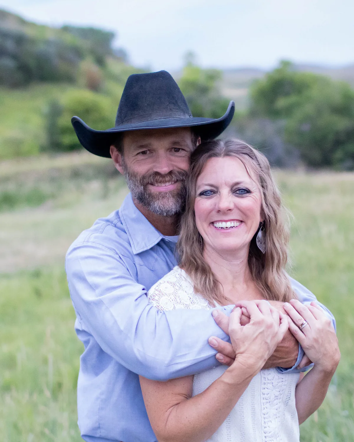 Paul Van Dyke in a black cowboy hat with his arms around Amber, standing in a green Wyoming meadow