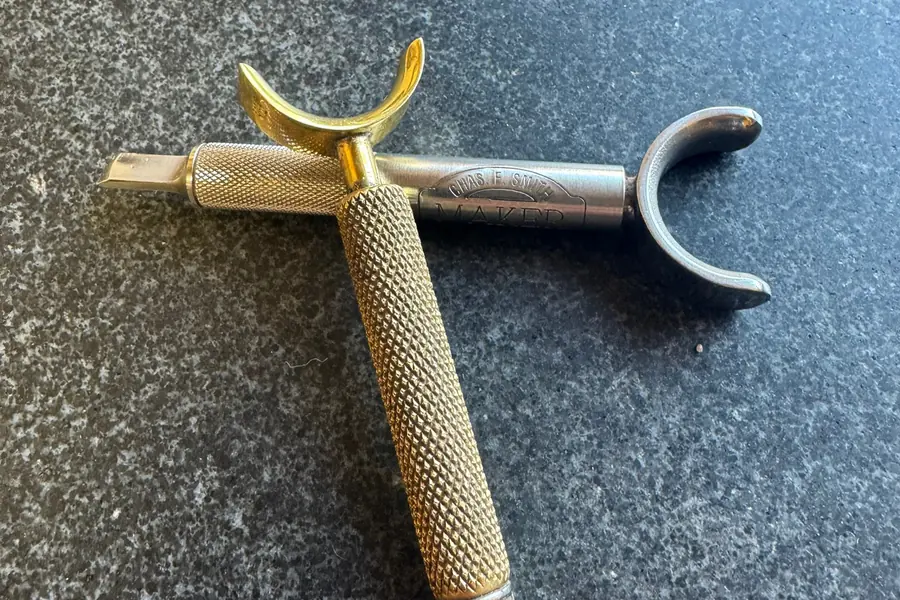 Two swivel knives, one with a knurled brass barrel, crossed on a granite bench top