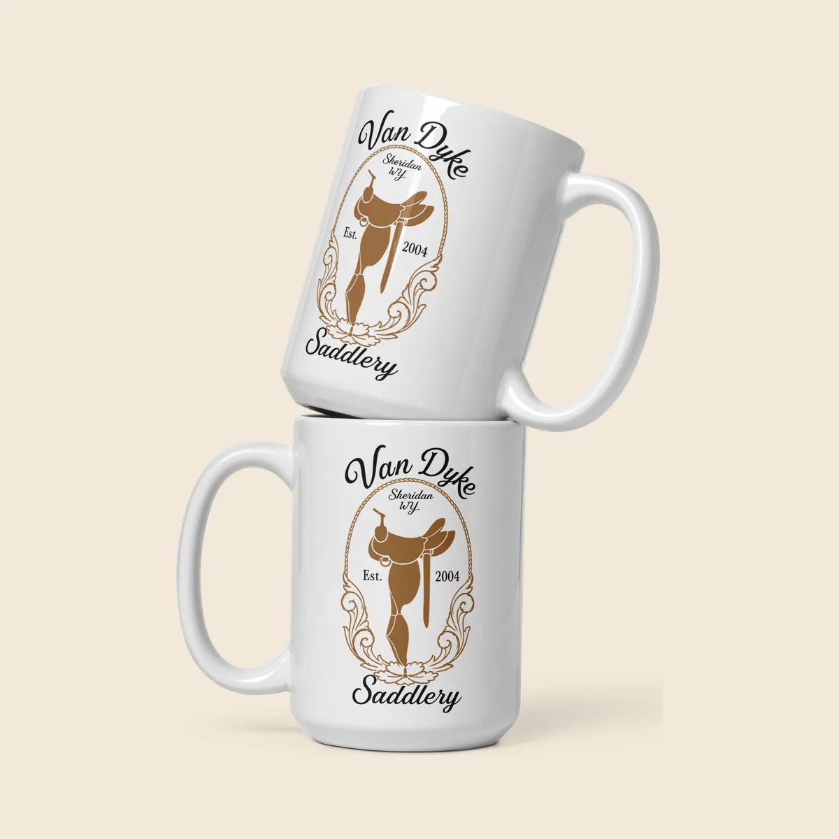 Two white glossy Van Dyke Saddlery mugs stacked, each with the saddle mark printed in tan