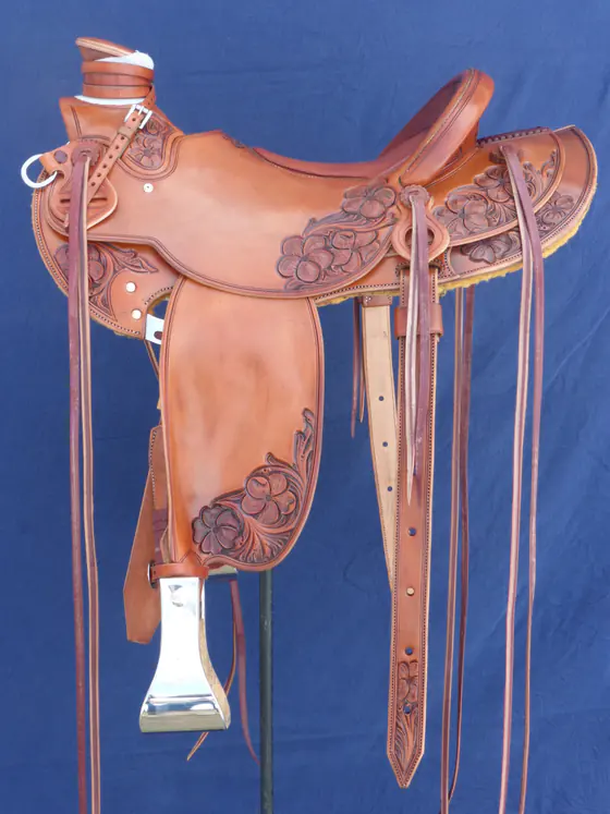 Smooth-seat custom saddle with carved floral corners and fender tips, against a blue backdrop