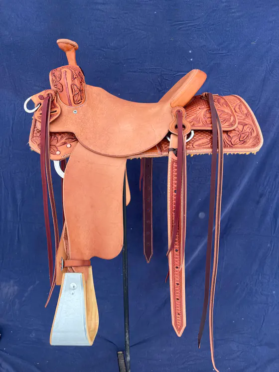 Roughout custom saddle with basket stamping and floral corners on the skirts, photographed against a blue backdrop