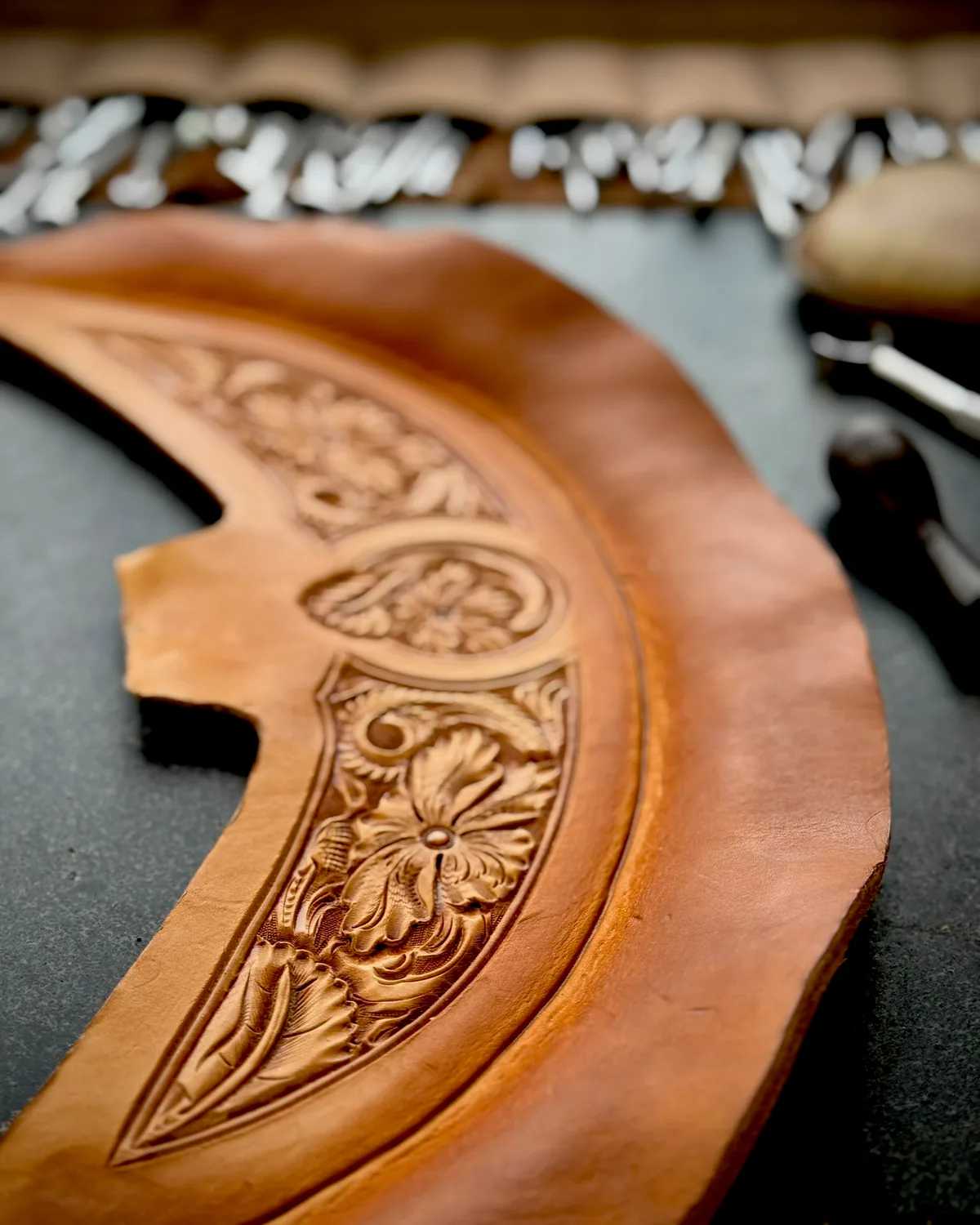 A hand-carved floral cantle piece in progress on the bench, with a rack of stamping tools behind it