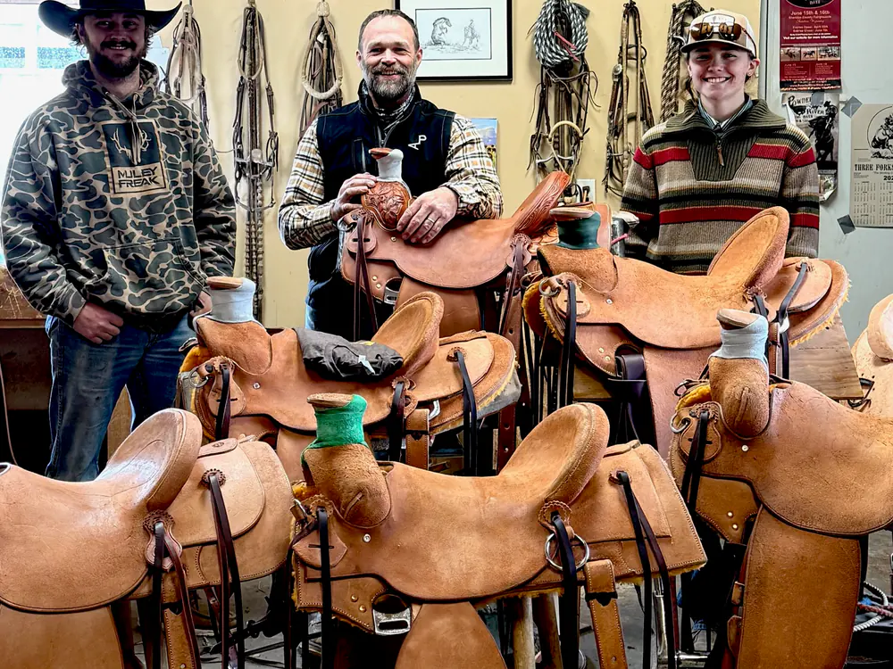 Paul Van Dyke and two students in a shop full of student-built saddles